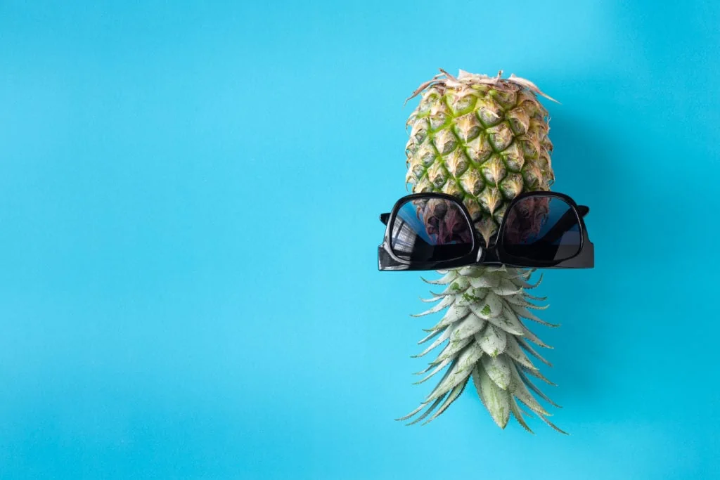 Ananas à l'envers sur fond bleu avec des lunettes de soleil