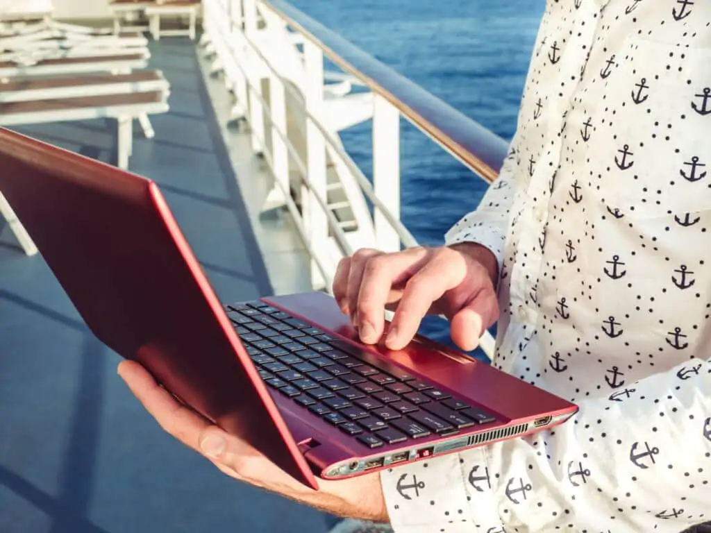 Homme sur le balcon d’un bateau de croisière utilisant son ordinateur portable rouge