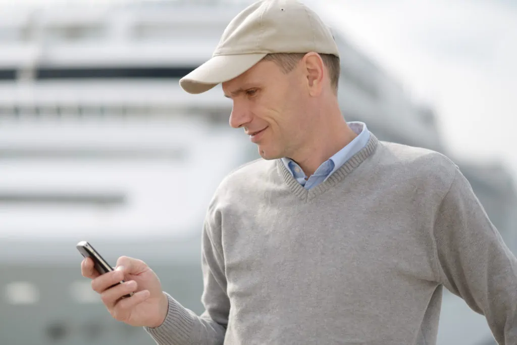 Touriste lisant un message texte sur son téléphone portable avec un bateau de croisière en arrière-plan