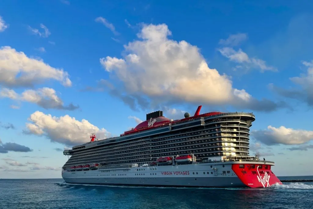 Le navire de croisière Virgin Voyages Scarlet Lady quitte le port de Miami au coucher du soleil pour une croisière sur l'océan Atlantique sous un ciel bleu avec quelques nuages