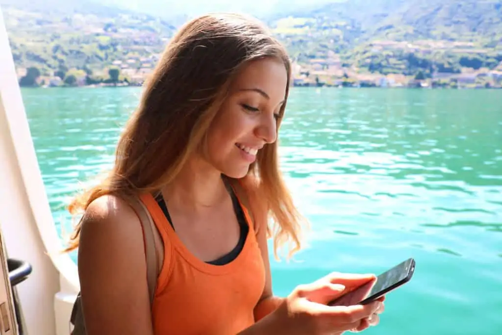 Femme sur son téléphone sur un bateau de croisière avec une île tropicale en arrière-plan