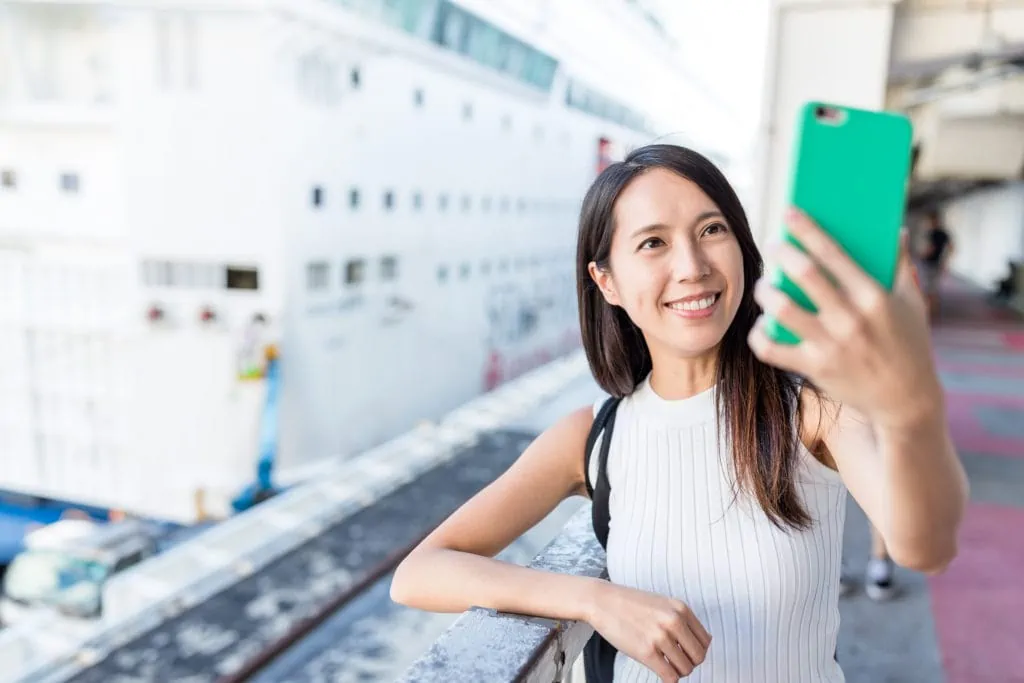 Femme utilisant son téléphone portable au port avec un bateau de croisière en arrière-plan